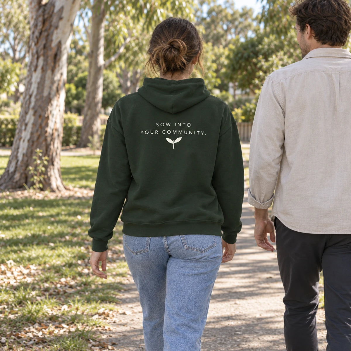A woman walking in the Forest Green Sowstead Core Hoodie, showing the back message, Sow into your community, and sprout artwork.